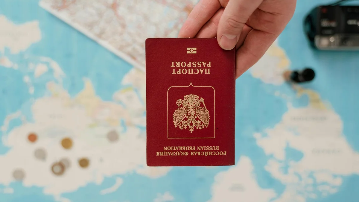 Pasaporte y documentos de seguro de viaje junto a maleta y estetoscopio sobre mesa de madera